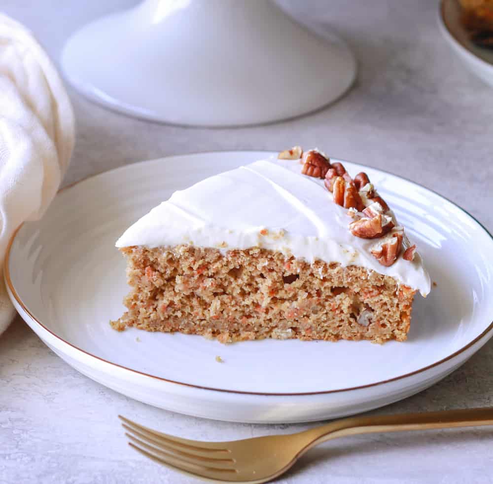 Pictured is a slice of healthy carrot cake made with oat flour on a white plate. 