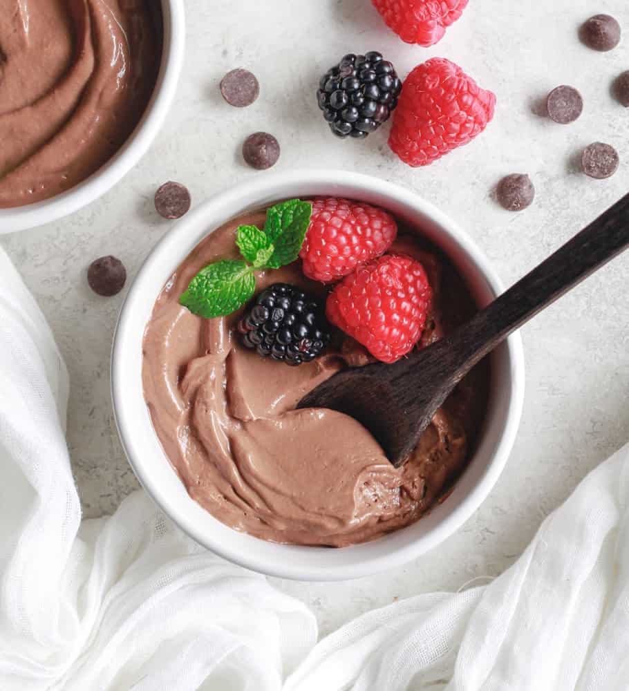 chocolate protein mousse in a white bowl garnished with berries and mint