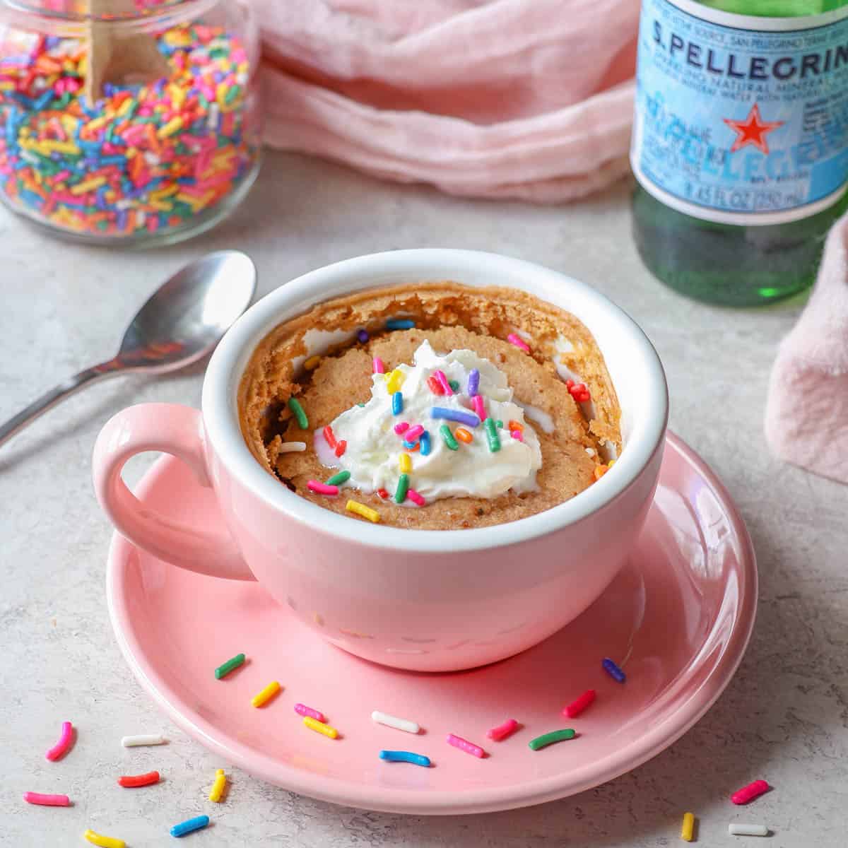 oat flour mug cake in a pink mug topped with whipped cream and sprinkles