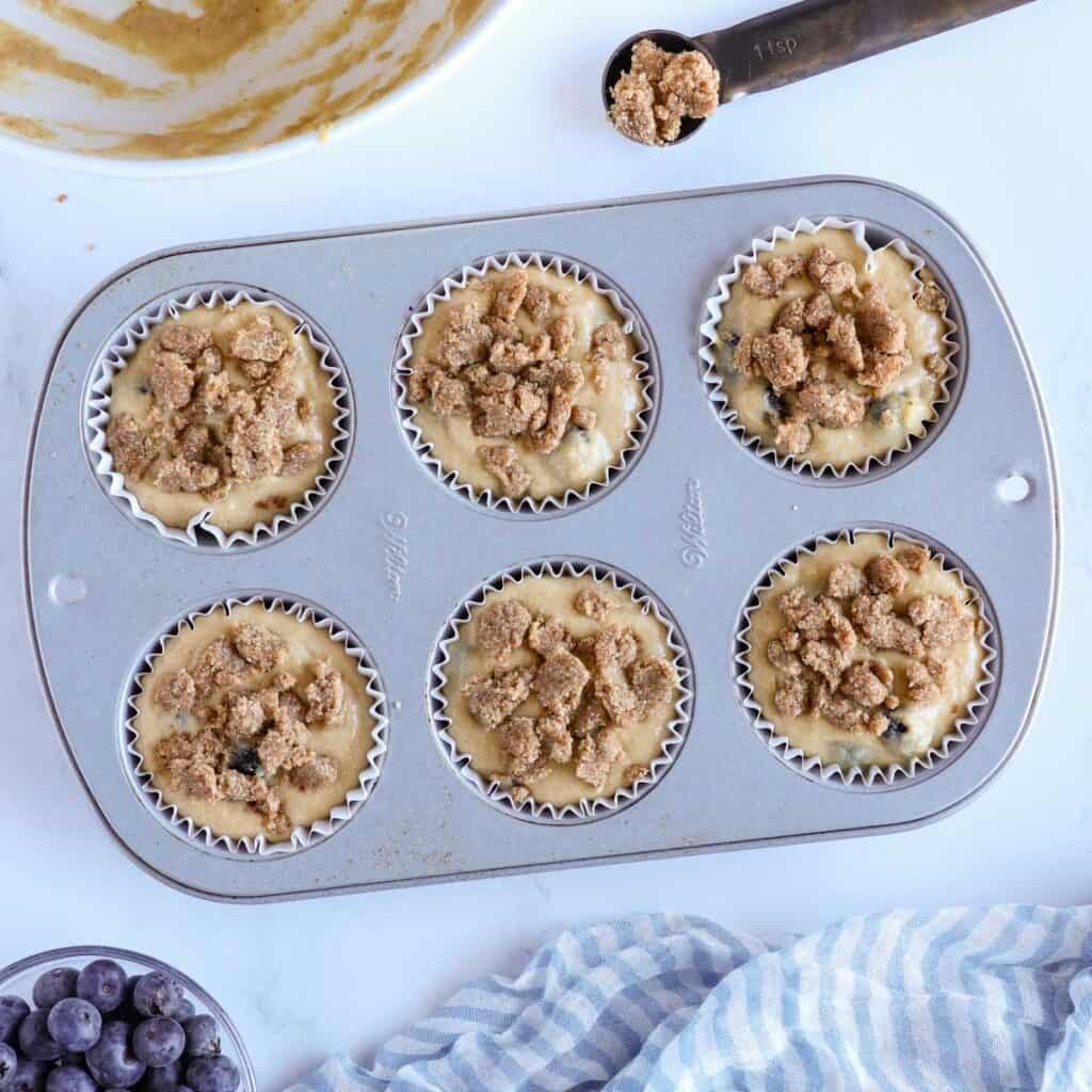 muffin batter in a muffin tray with crumb topping before being baked