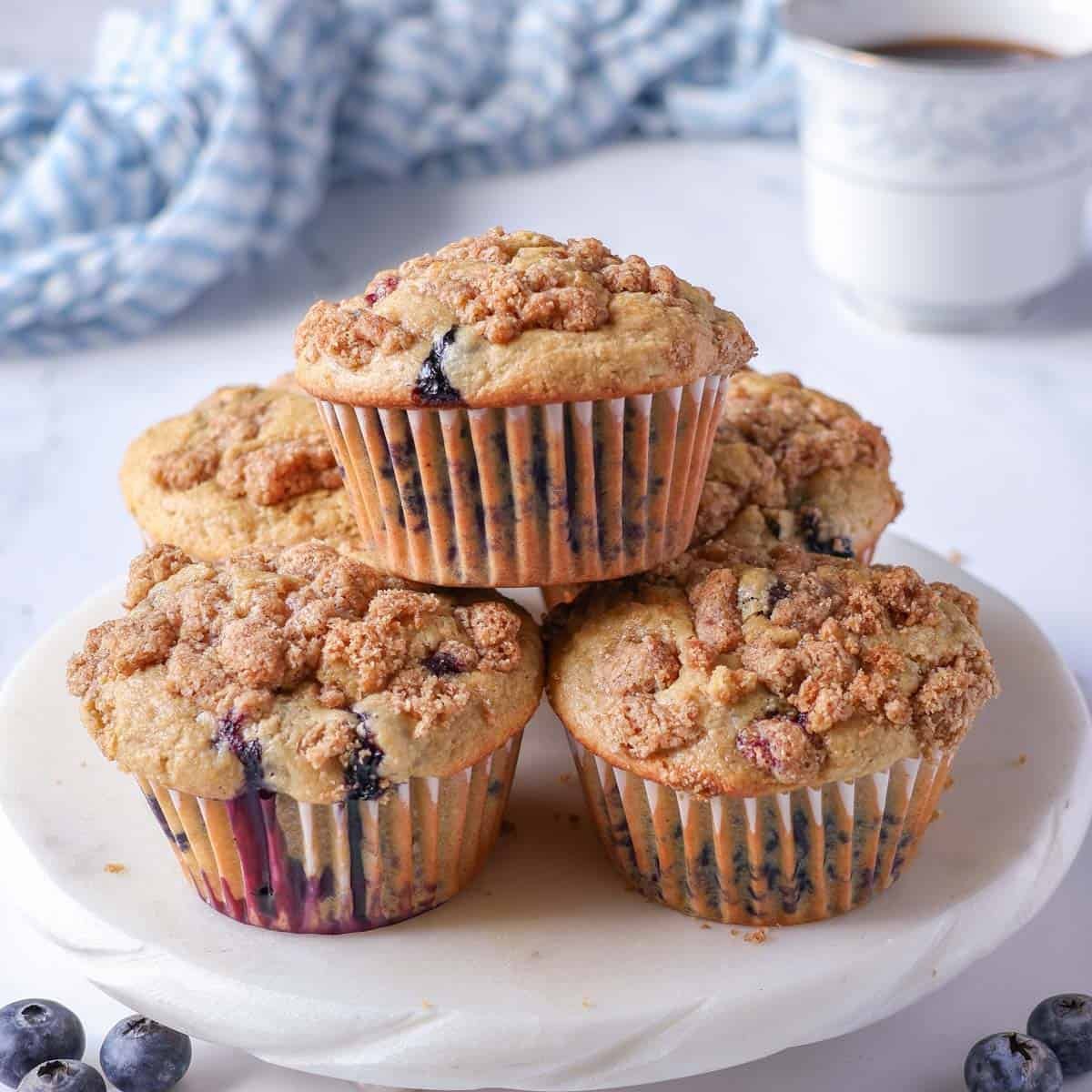 bakery-style oat flour blueberry muffins with crumb topping on a white serving plate