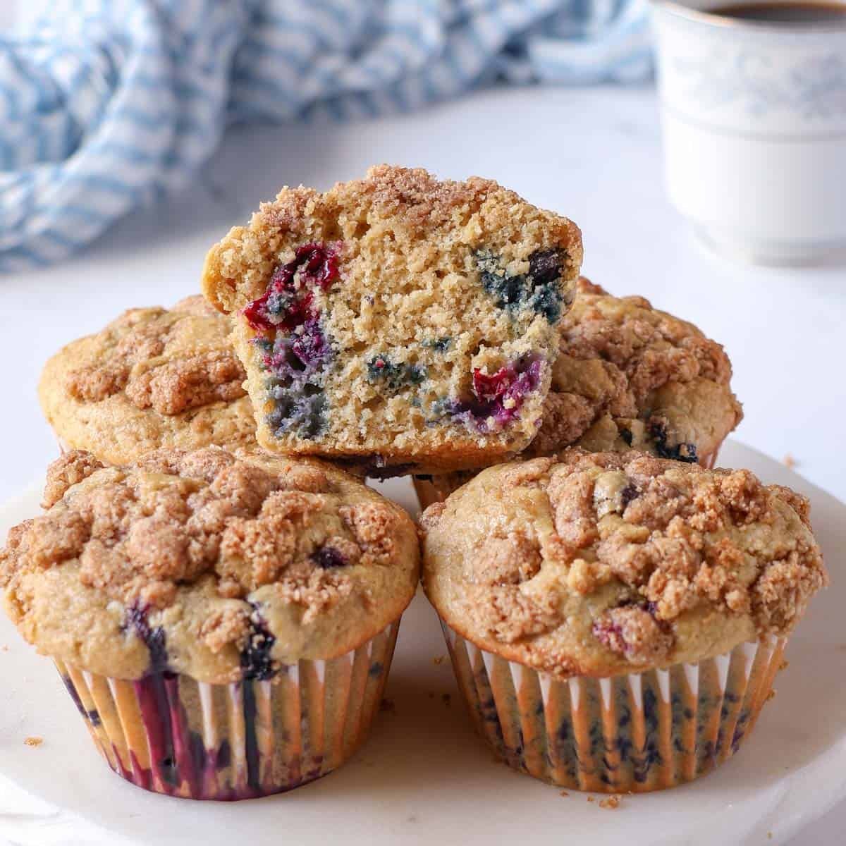 a stack of oat flour blueberry muffins, one cut open to show the crumb