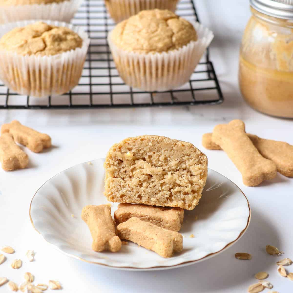 A peanut butter oat dog muffin cut in half to show the center on a white plate with three dog treats.